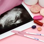 A closeup of pregnancy tests and an ultrasound with supplements on a pink background.