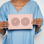 Healthcare professional holding a sign with breast shapes promoting breast cancer awareness.